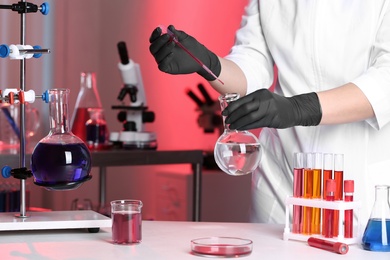 Photo of Scientist pouring reagent into flask at table in chemistry laboratory