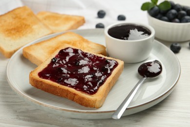 Photo of Toasts served with blueberry jam on white wooden table, closeup