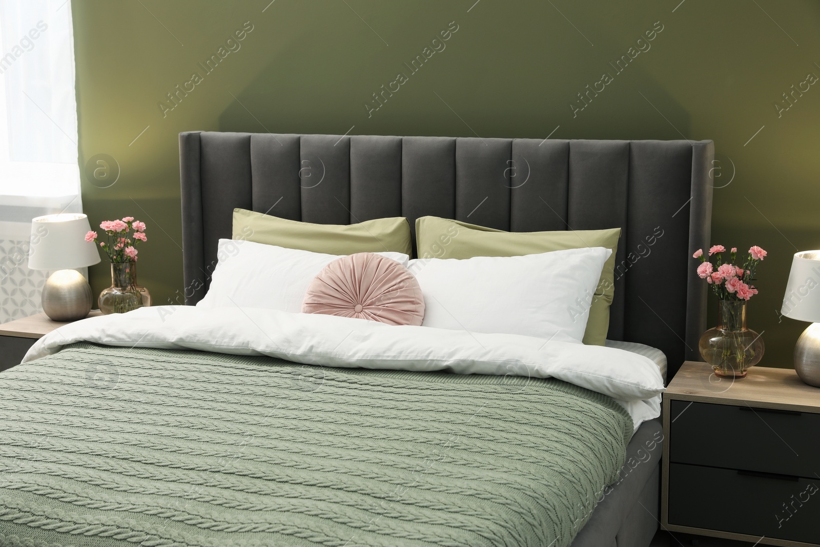 Photo of Large comfortable bed, lamps and beautiful flowers in stylish room. Interior design