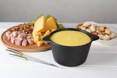 Photo of Fondue with tasty melted cheese, forks and different products on white wooden table