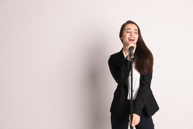 Young woman singing in microphone on color background. Space for text