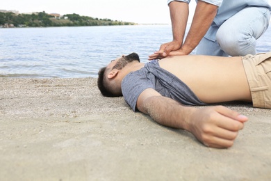 Passerby performing CPR on unconscious young man near sea. First aid