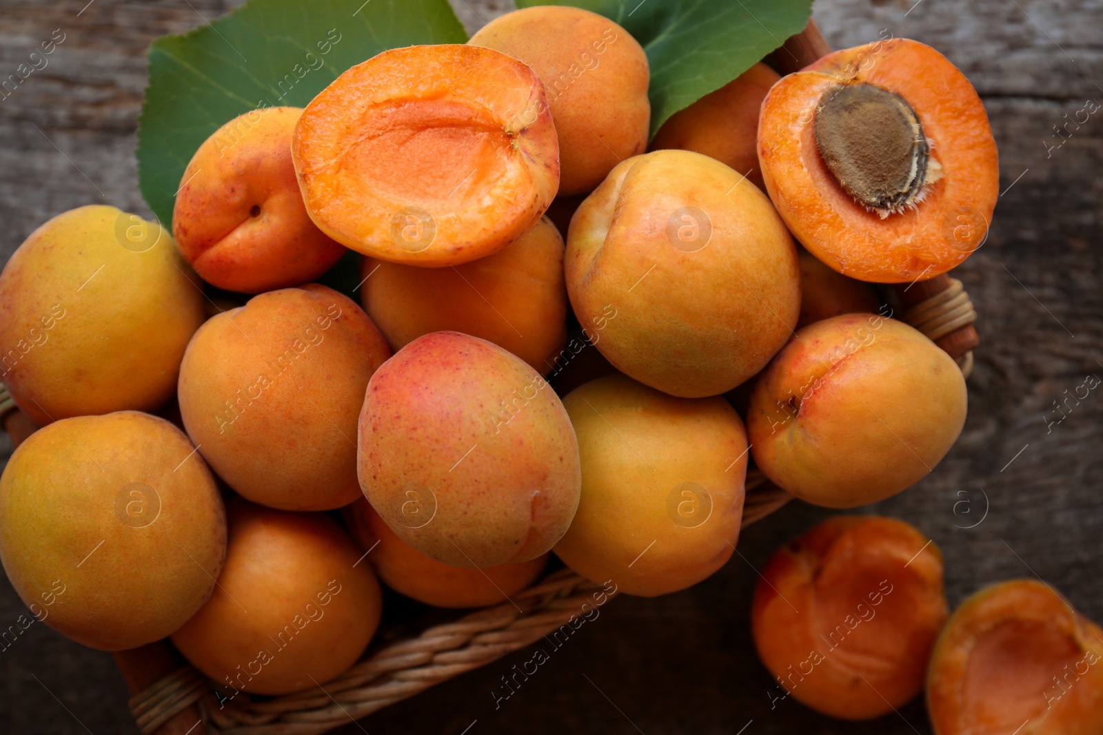 Photo of Basket with delicious ripe apricots on wooden table, top view