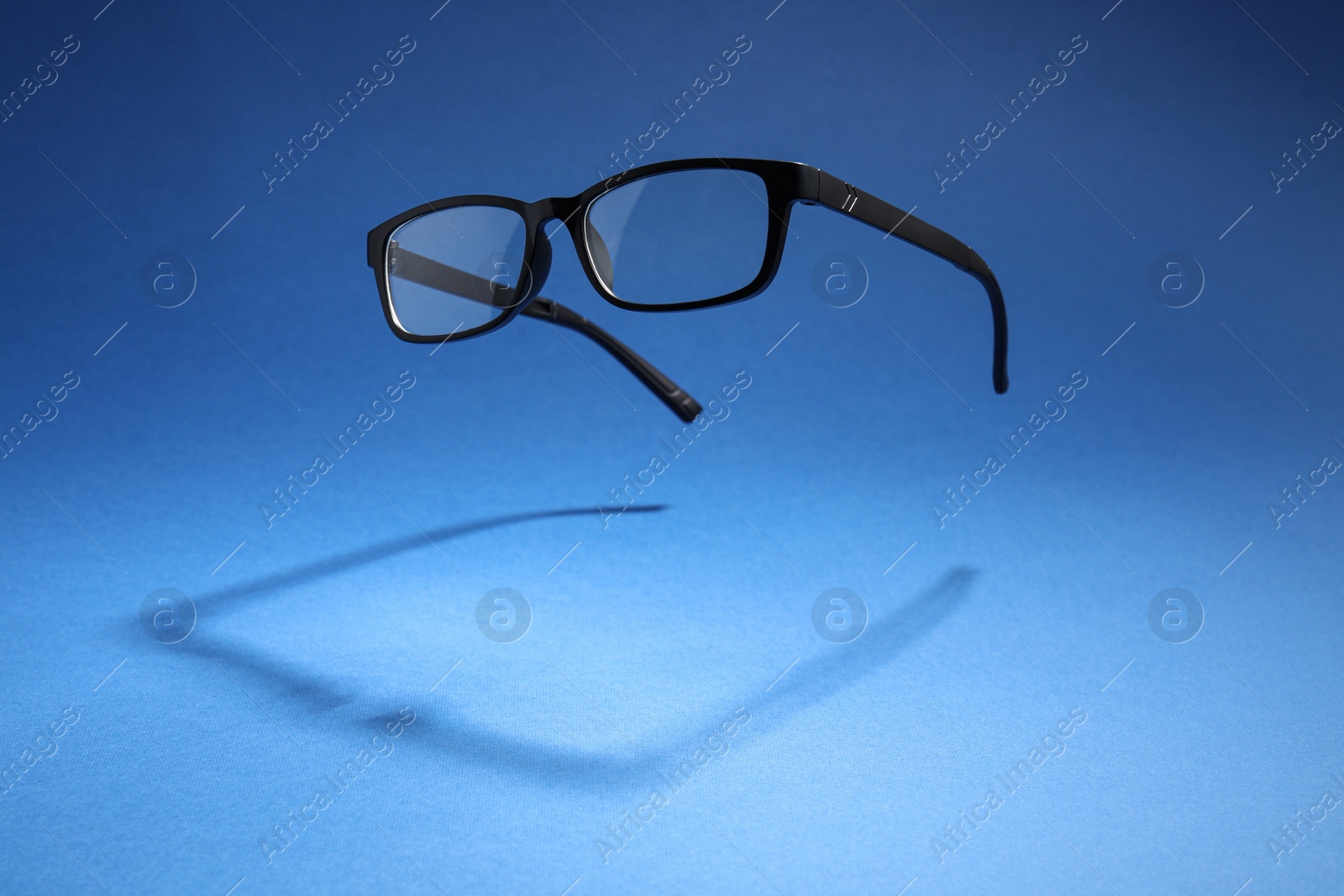 Photo of Stylish pair of glasses with black frame on blue background, space for text