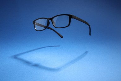 Photo of Stylish pair of glasses with black frame on blue background, space for text