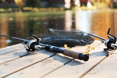 Photo of Fishing rods and fresh fish on wooden pier near pond