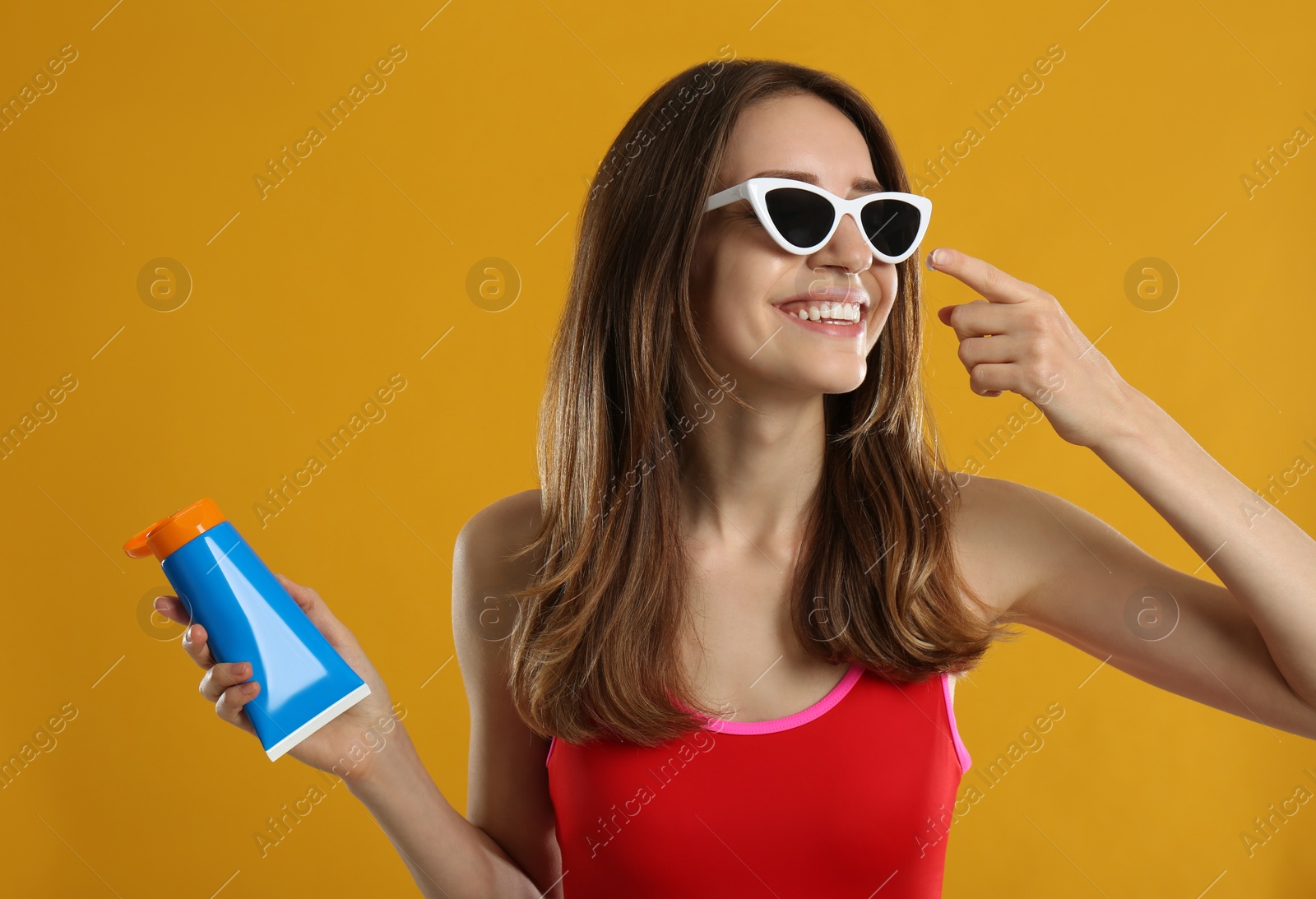 Photo of Young woman applying sun protection cream on orange background