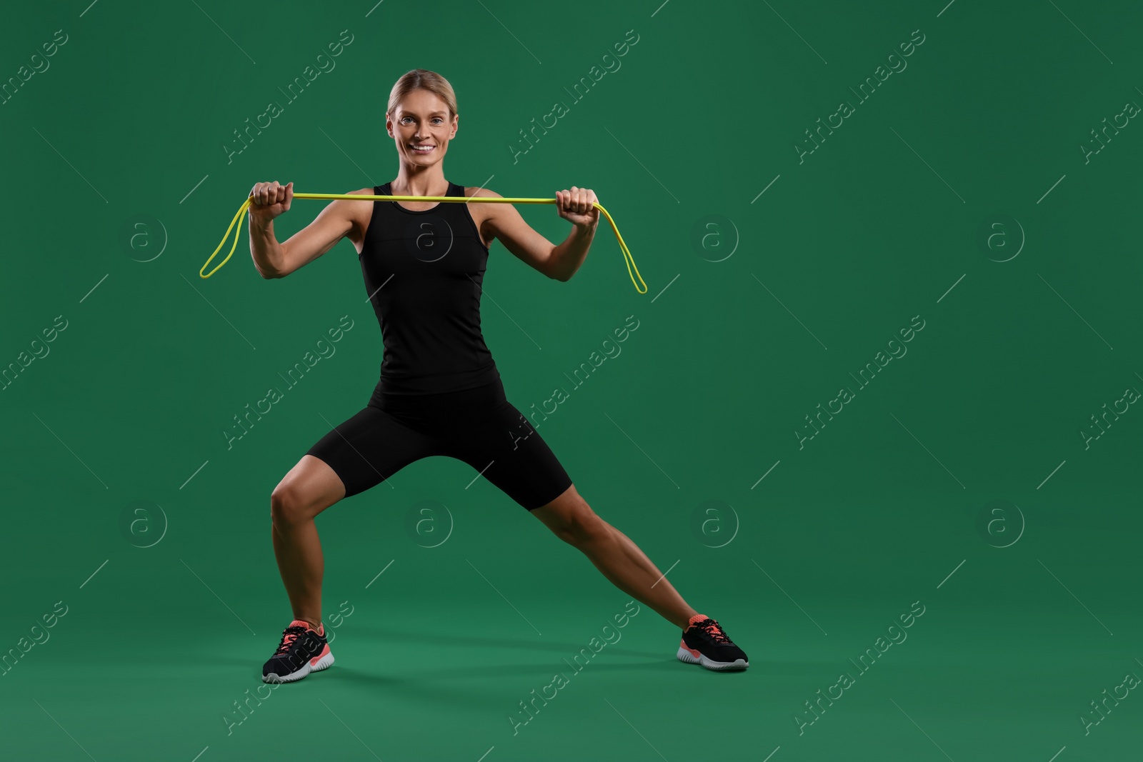 Photo of Smiling woman exercising with elastic resistance band on green background. Space for text