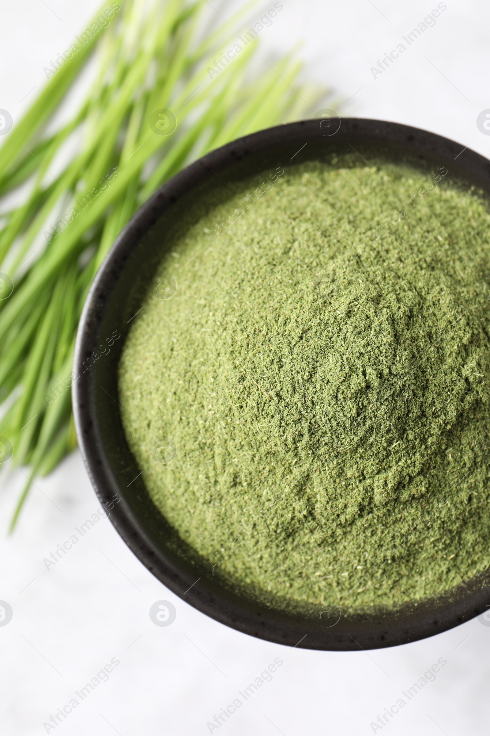 Photo of Wheat grass powder in bowl on white table, top view