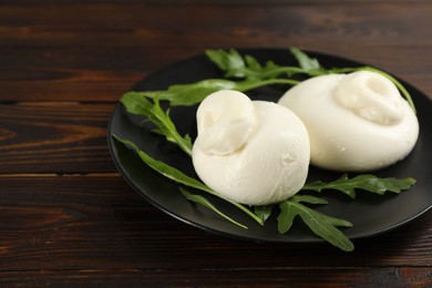 Photo of Delicious burrata cheese with arugula on wooden table, closeup