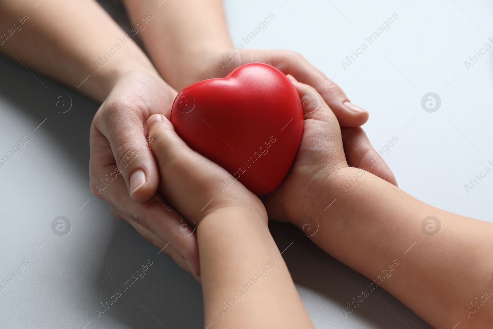 Photo of Mother and her child holding red decorative heart on gray background, closeup