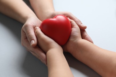 Mother and her child holding red decorative heart on gray background, closeup