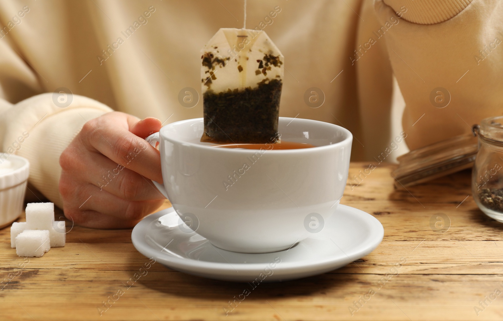 Photo of Tea brewing. Woman putting tea bag into cup at wooden table, closeup