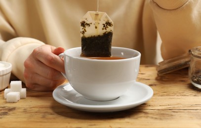 Photo of Tea brewing. Woman putting tea bag into cup at wooden table, closeup