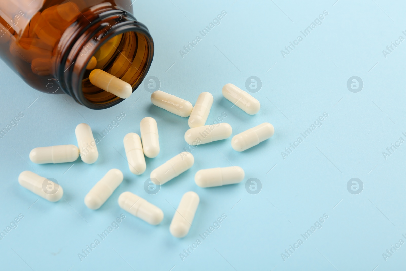 Photo of Bottle and vitamin capsules on light blue background, closeup. Space for text