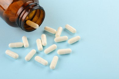 Bottle and vitamin capsules on light blue background, closeup. Space for text