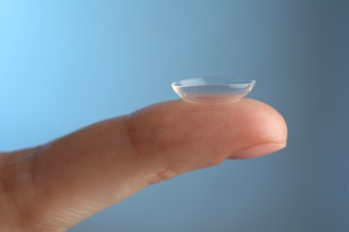 Photo of Woman holding contact lens on light blue background, closeup