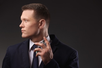 Photo of Handsome man in suit using perfume on dark background