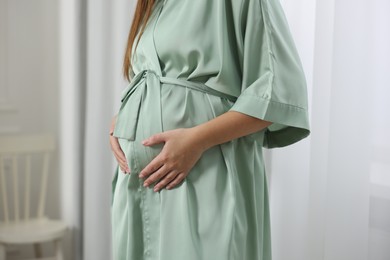 Photo of Pregnant woman in green dressing gown near window indoors, closeup