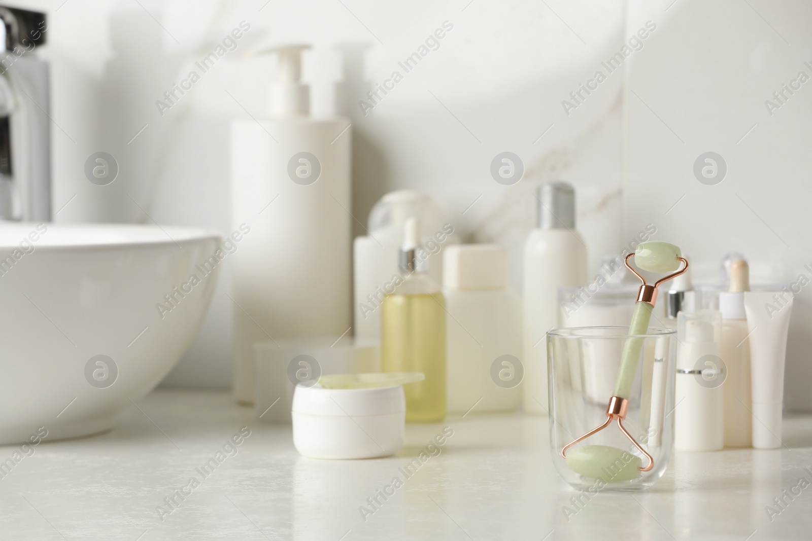 Photo of Natural face roller, gua sha tool and cosmetic products on counter in bathroom