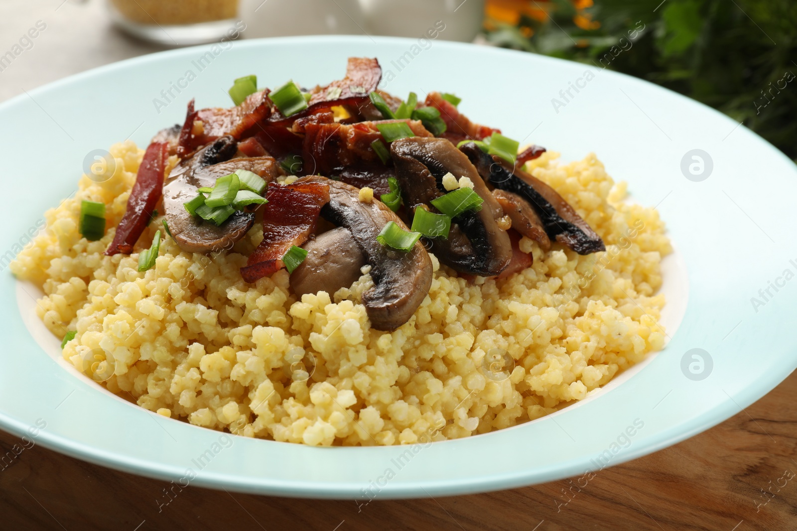 Photo of Tasty millet porridge with mushrooms, bacon and green onion on table, closeup