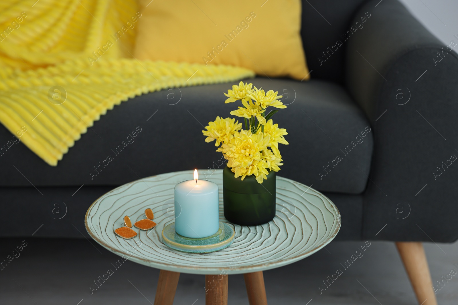 Photo of Side table with candle, flowers and earrings near sofa in room. Interior design