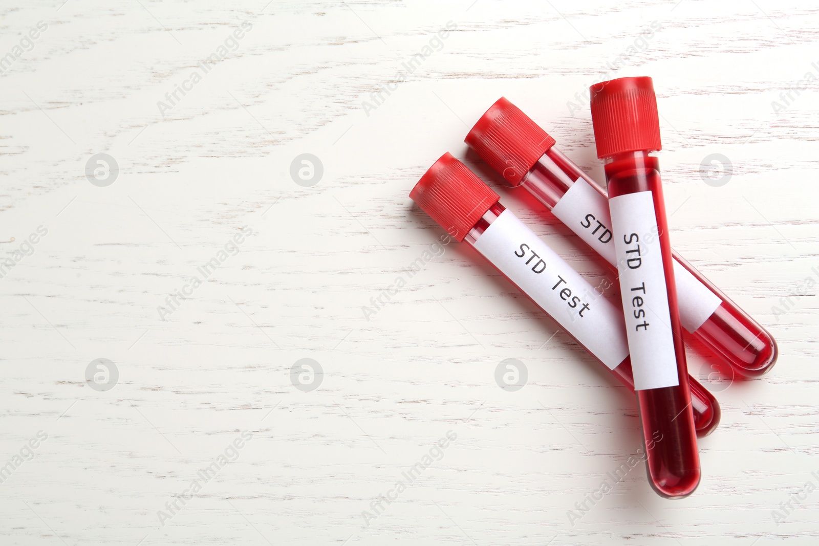 Photo of Tubes with blood samples and labels STD Test on white wooden table, flat lay. Space for text