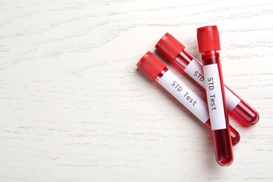 Tubes with blood samples and labels STD Test on white wooden table, flat lay. Space for text