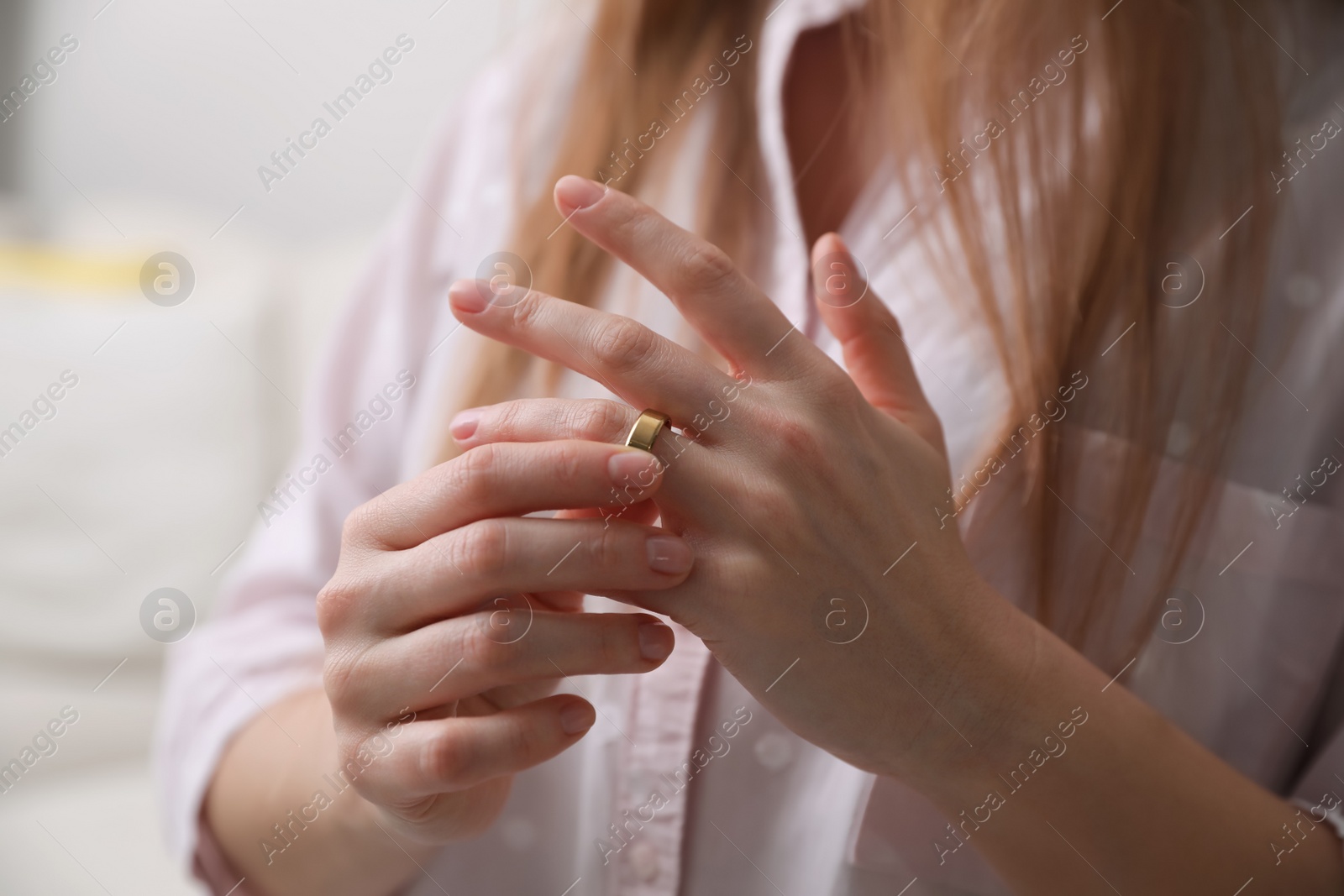 Photo of Woman taking off wedding ring indoors, closeup. Divorce concept