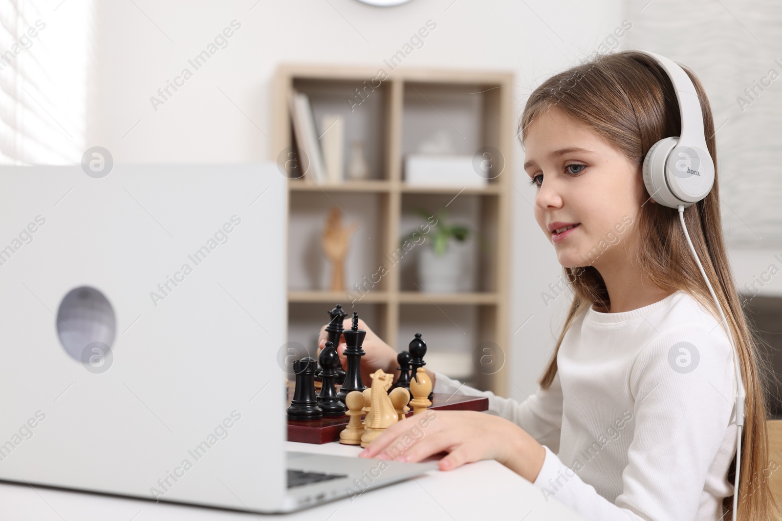 Photo of Cute girl learning to play chess with online tutor at home