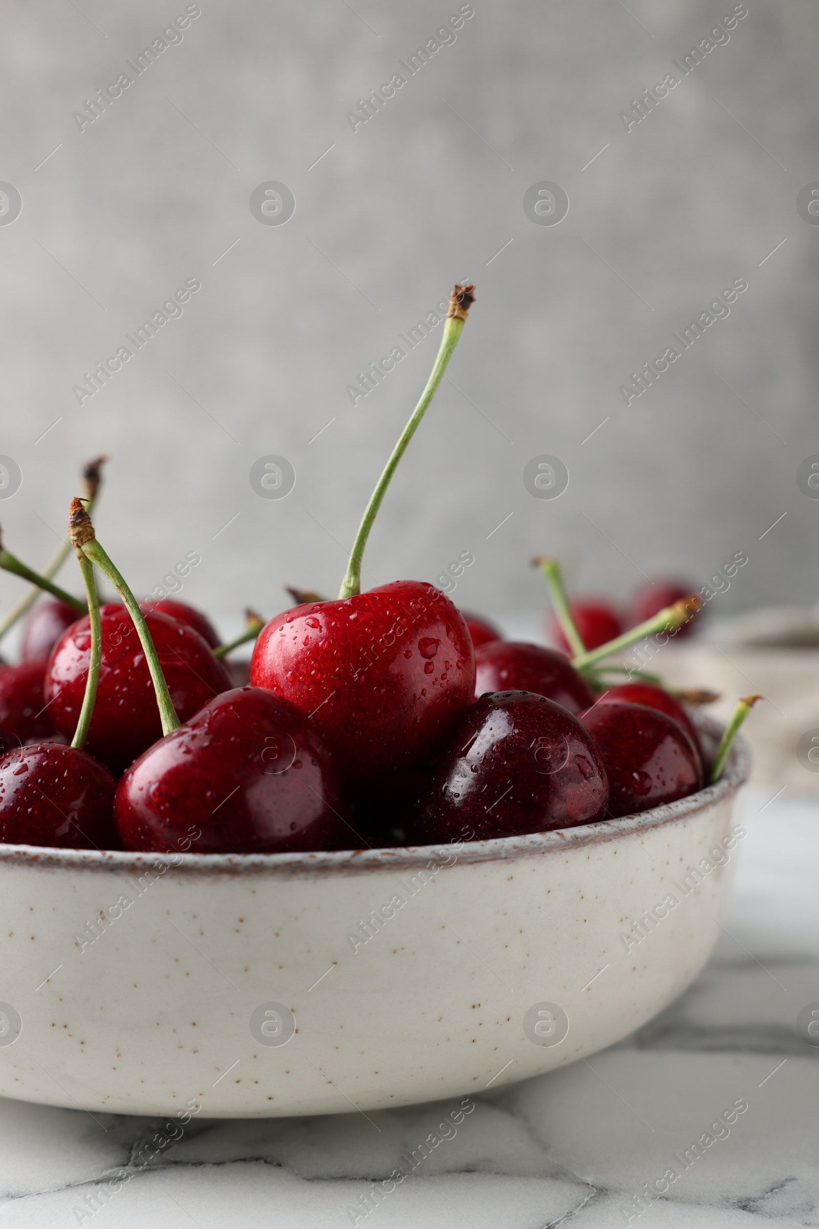 Photo of Fresh ripe cherries with water drops in bowl on white marble table, closeup