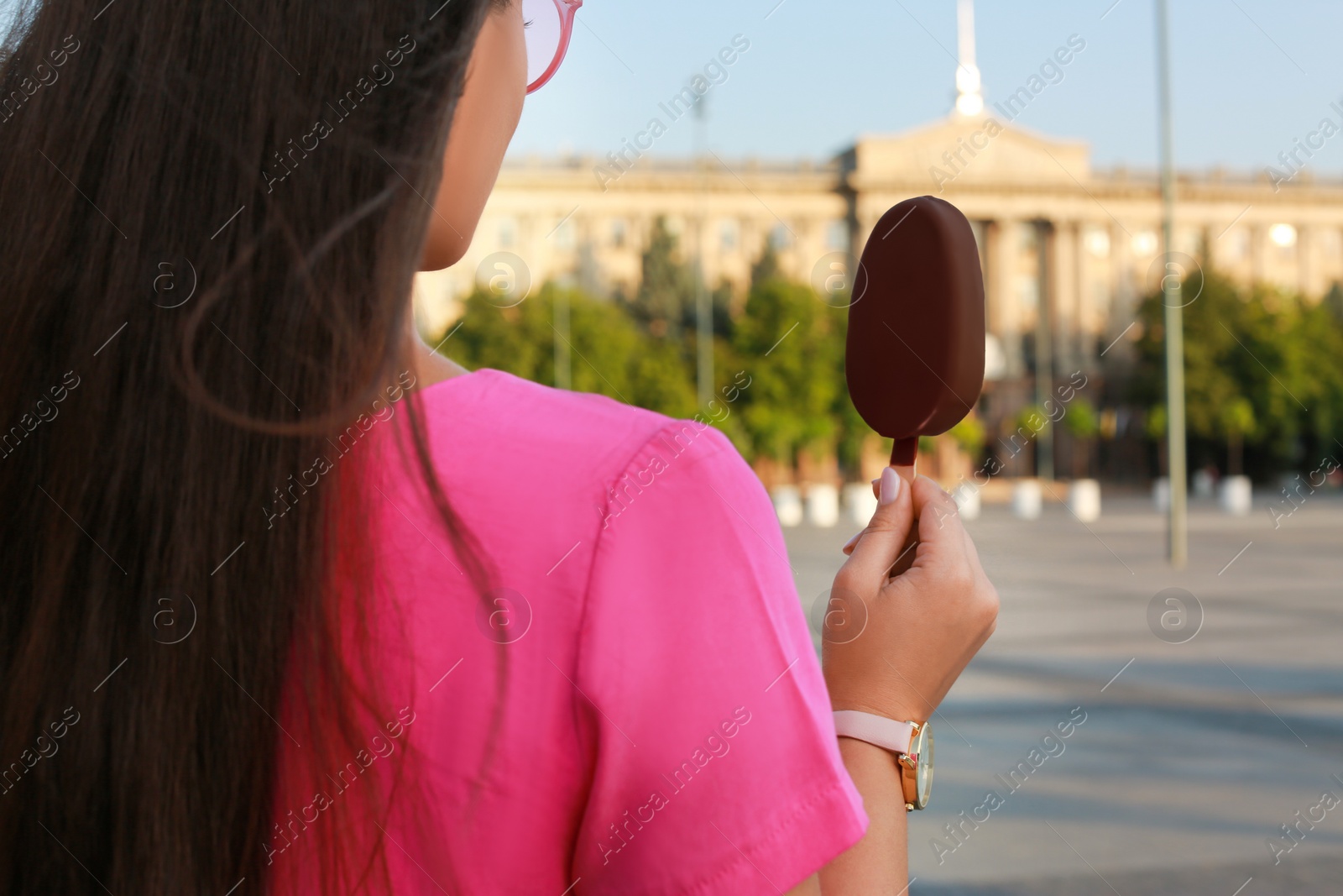 Photo of Young woman holding ice cream glazed in chocolate on city street, closeup