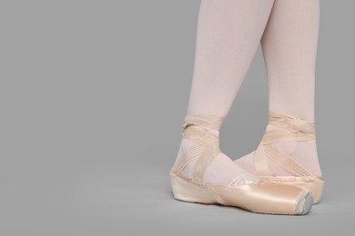 Young ballerina in pointe shoes practicing dance moves on grey background, closeup. Space for text