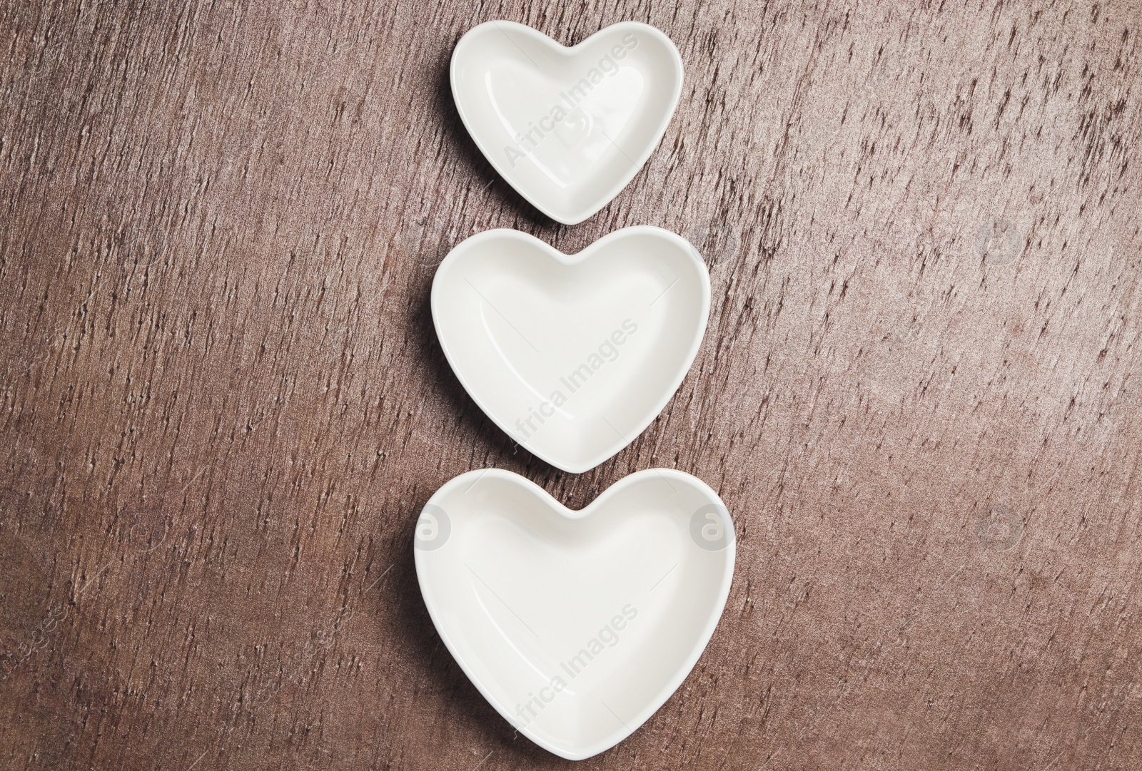 Photo of Heart shaped baking dishes on wooden table, flat lay. Cooking utensils