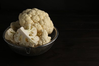 Photo of Colander with fresh raw cauliflower on black wooden table. Space for text