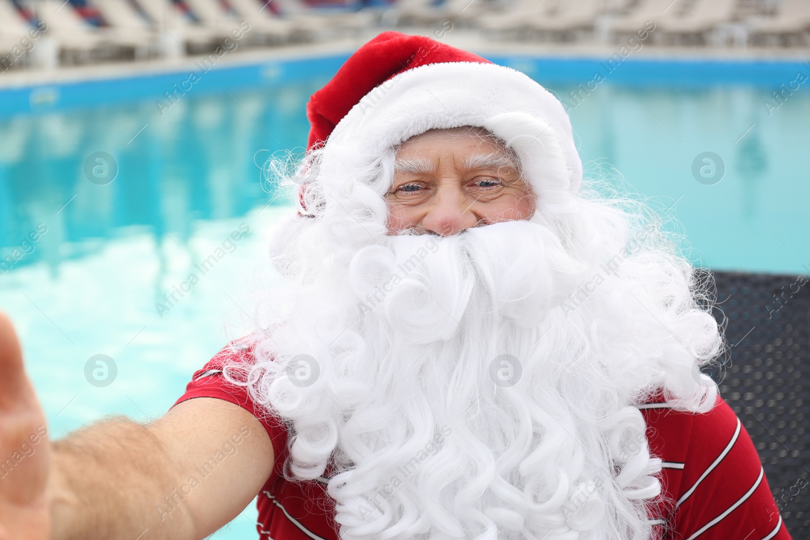 Photo of Authentic Santa Claus taking selfie near swimming pool outdoors