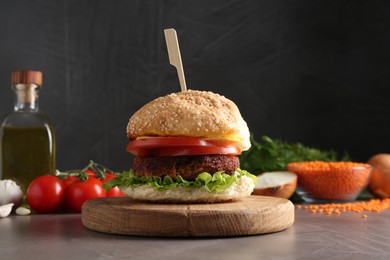 Photo of Board with delicious vegetarian burger on grey textured table