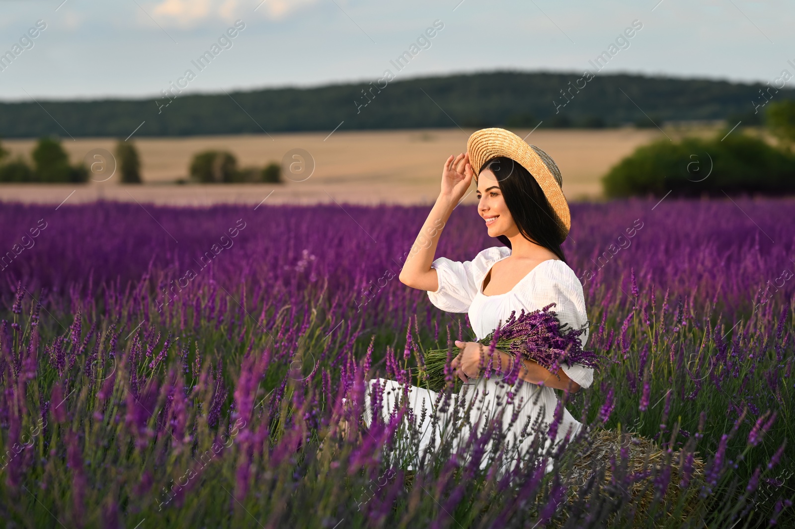 Photo of Beautiful young woman with bouquet sitting in lavender field