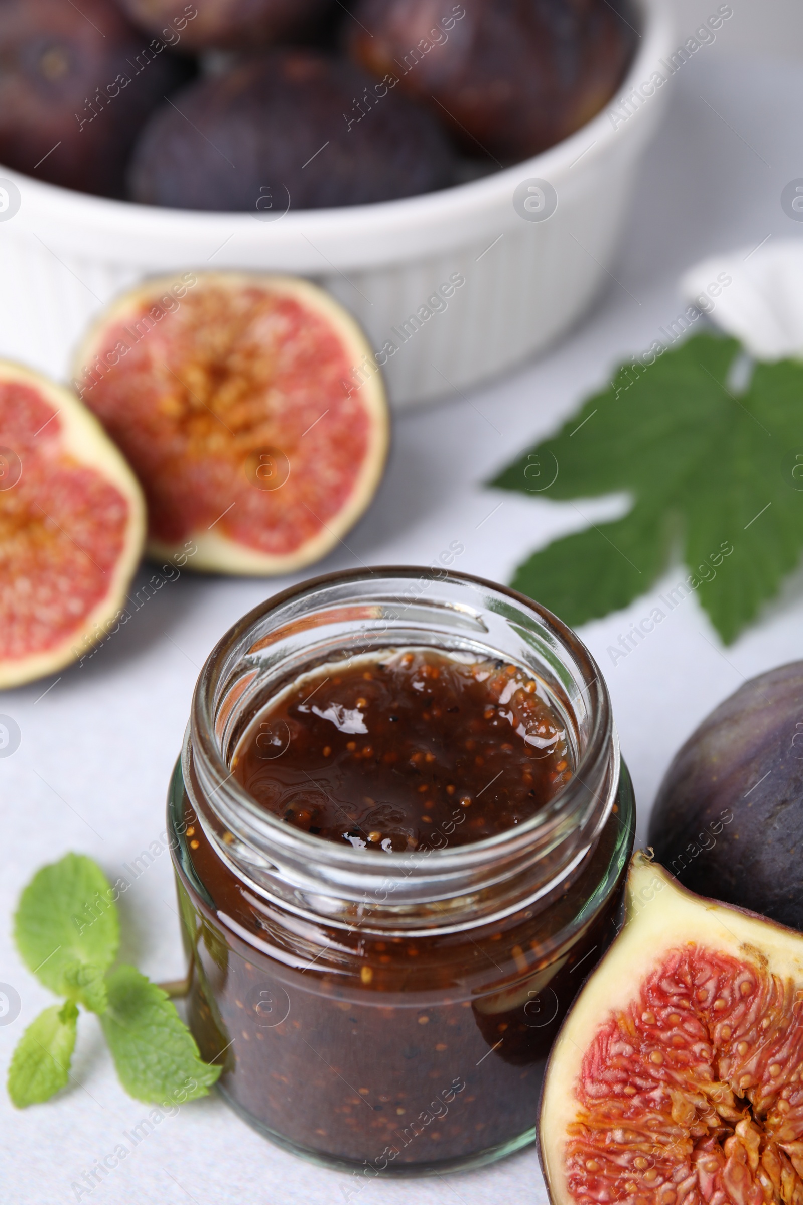 Photo of Glass jar of tasty sweet fig jam and fruits on light table