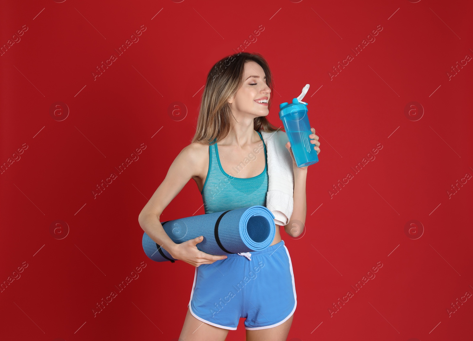 Photo of Beautiful woman with yoga mat, towel and shaker on red background