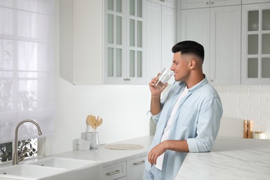 Man drinking tap water from glass in kitchen