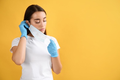 Photo of Woman in medical gloves putting on protective face mask against yellow background. Space for text