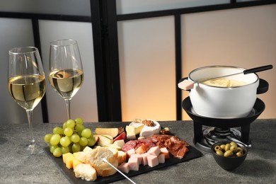 Photo of Fork with piece of ham, fondue pot with melted cheese, wine and snacks on grey table