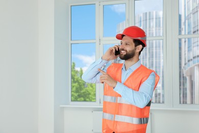 Man in reflective uniform talking on phone indoors, space for text