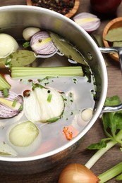 Pot and different ingredients for cooking tasty bouillon on wooden table, above view