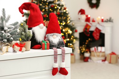 Photo of Funny Christmas gnomes on commode in room with festive decoration. Space for text