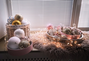Photo of Beautiful Christmas tree baubles and fairy lights on window sill indoors