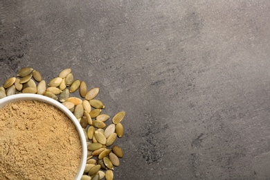 Bowl with pumpkin flour and seeds on grey background, top view. Space for text