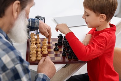 Grandfather and grandson playing chess at table indoors, closeup