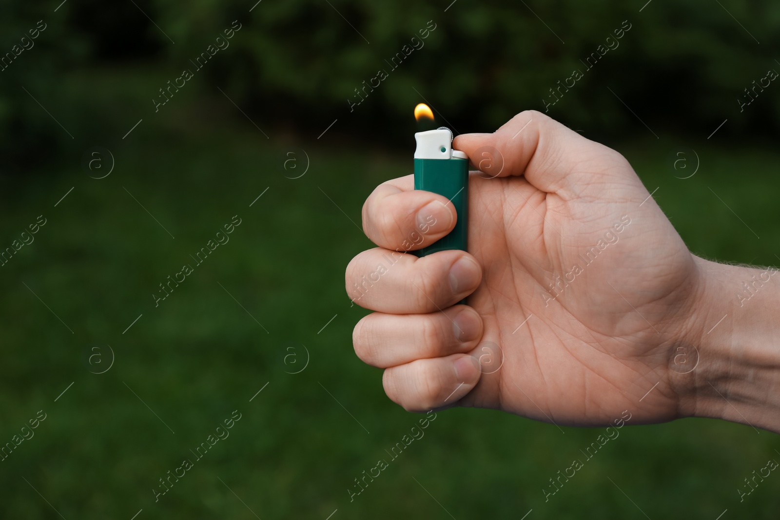 Photo of Man holding lighter with burning flame outdoors, closeup. Space for text